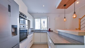 A modern kitchen with stainless steel appliances, a built-in oven, a water dispenser, and a wooden countertop. - Le Refuge Balnéaire - À 3km de la plage (Pornichet)