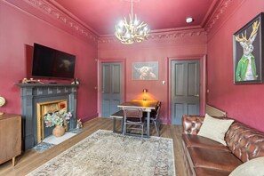 A living room with a fireplace, a television, a dining table with chairs, and a leather sofa. - Stylish Scottish 3-Bed | Heart of Stirling (Stirling)
