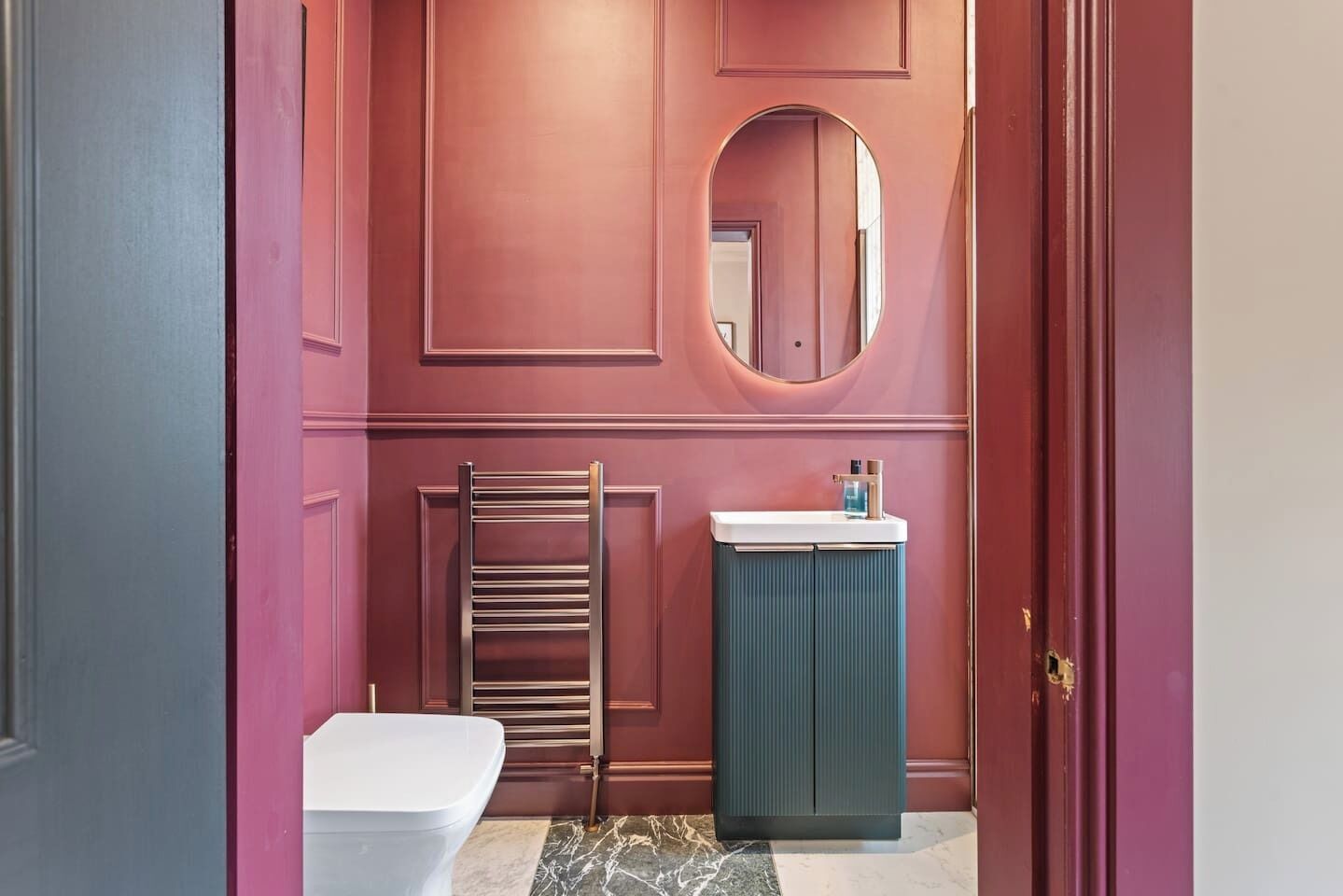 Une salle de bain avec des toilettes blanches, un porte-serviettes, un lavabo avec un miroir et un meuble bleu.