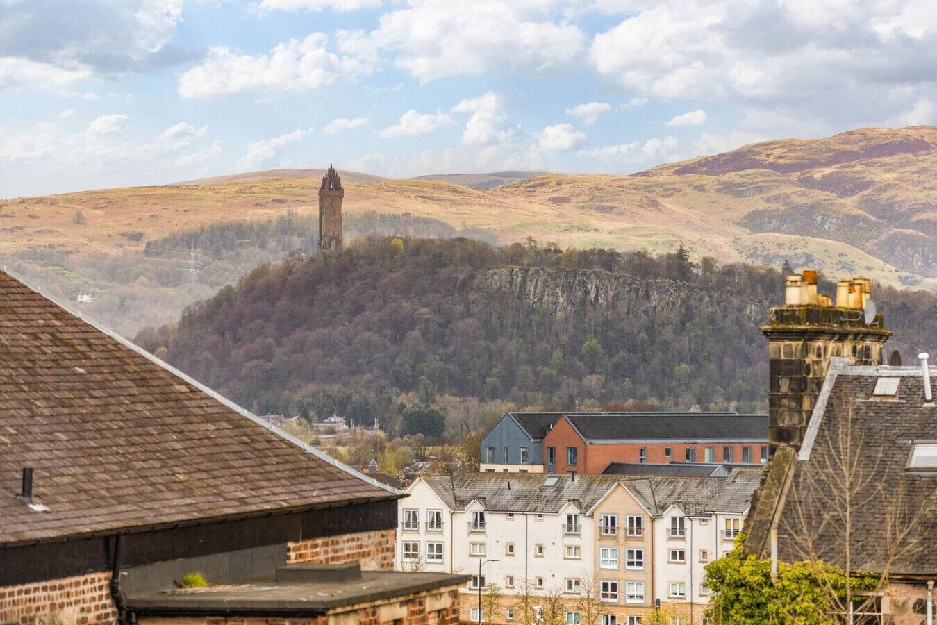 A town with a prominent tower, residential buildings, and a hilly landscape.