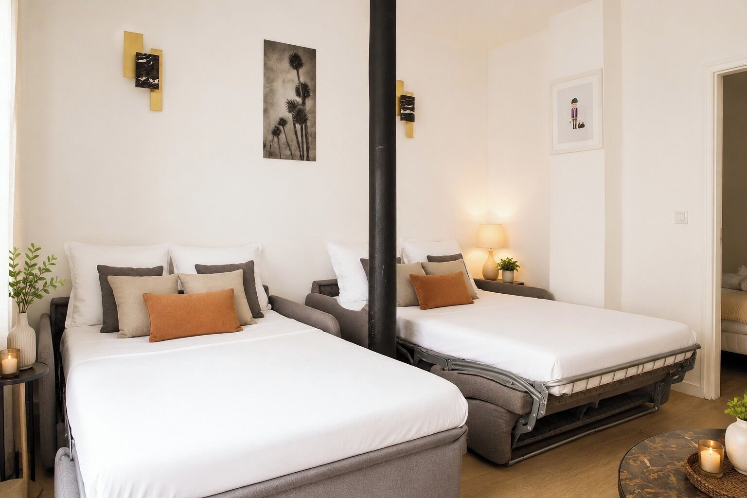 Een hotelkamer met twee bedden, nachtkastjes, een lamp, een kleine plant en kunstwerken aan de muur.
