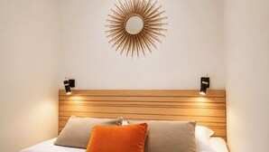 Ein Bett mit Holz-Kopfteil, zwei Wandlampen und einem Spiegel mit Sonnenstrahlendesign.