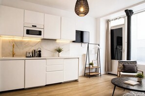 Uma cozinha moderna com armários brancos, forno embutido, televisão preta e piso de madeira.
