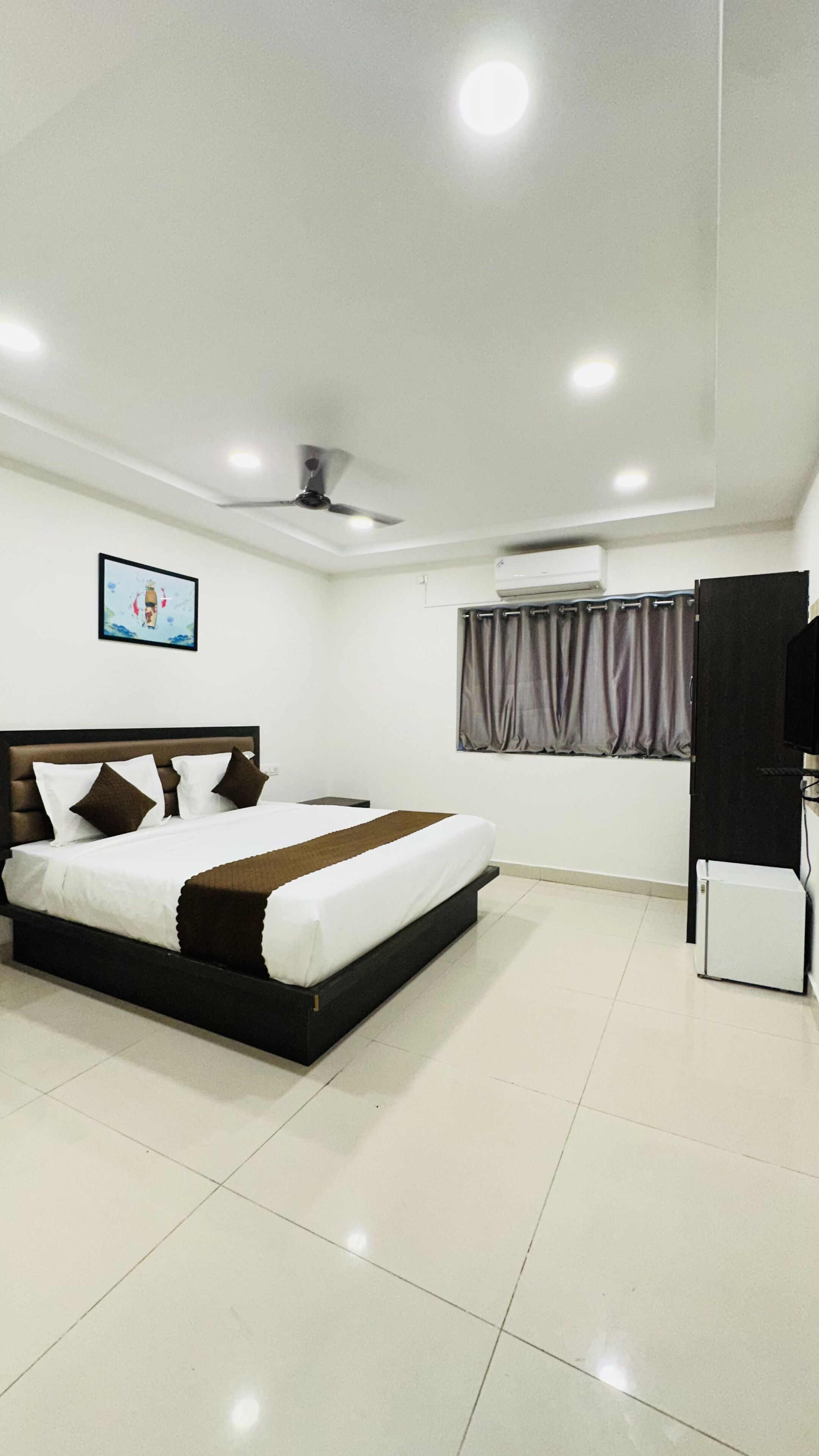 Une chambre à coucher avec un lit, un ventilateur de plafond, une fenêtre avec des rideaux et un meuble pour la télévision.