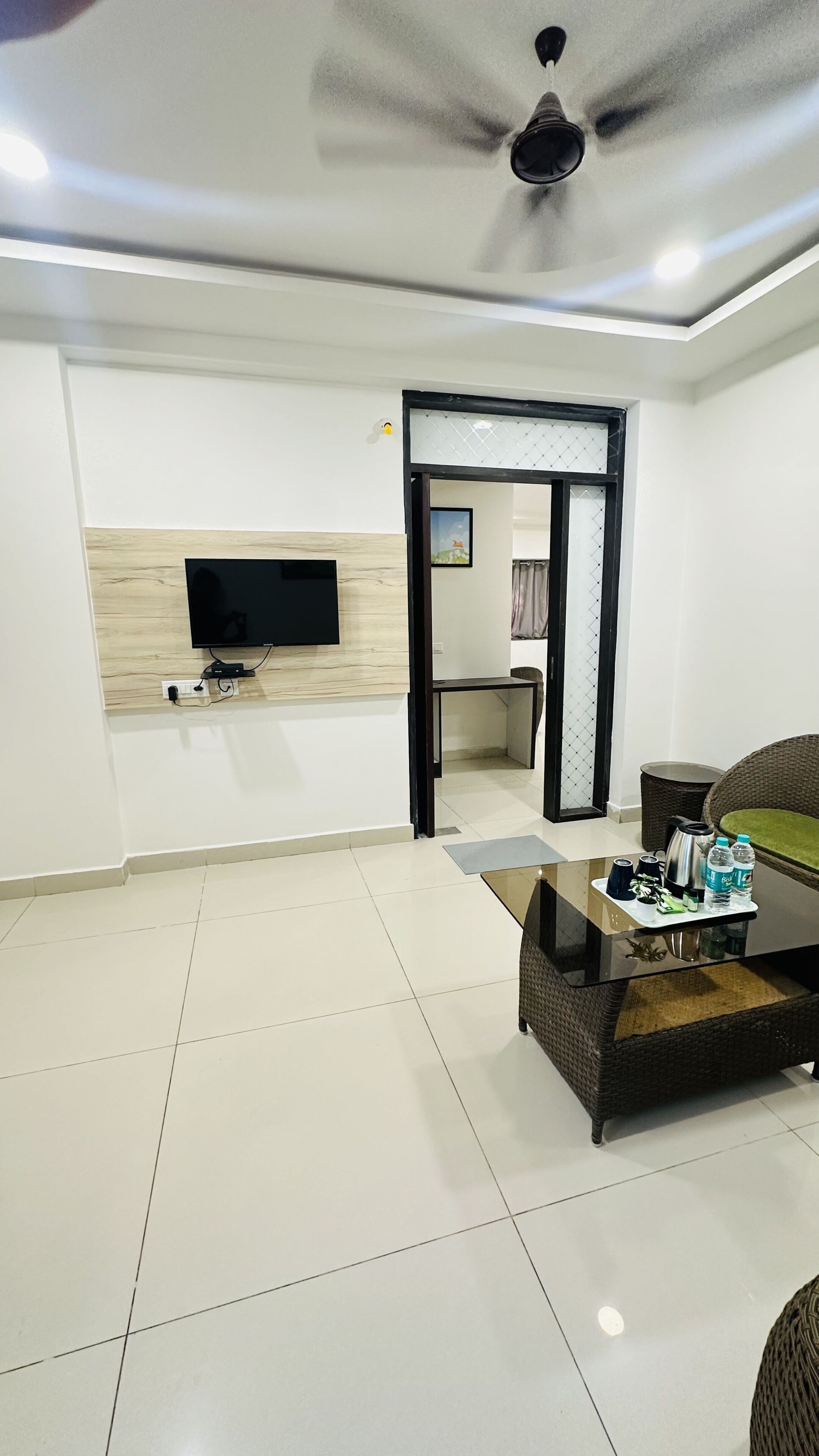 A living room with a flat-screen TV, a ceiling fan, a wicker coffee table, and a dining area with a table and chairs.