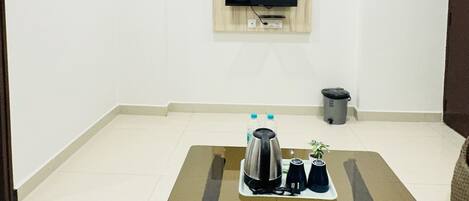 A modern living room with a glass-top coffee table, a ceiling fan, a mounted TV, and a trash bin.