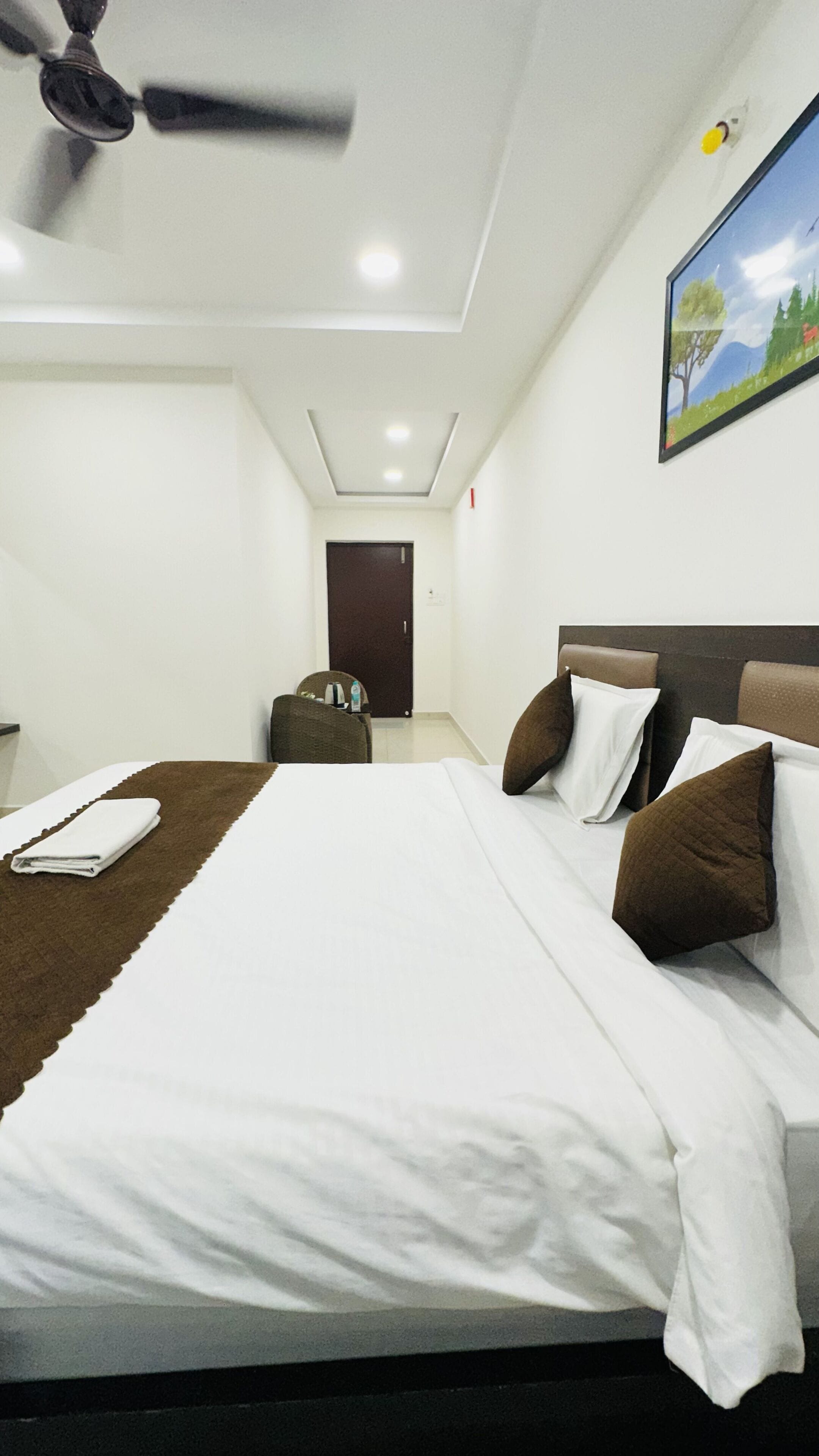A hotel room with a bed, a ceiling fan, a door, and a painting on the wall.