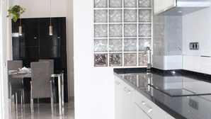 Een moderne keuken met een zwart aanrecht, roestvrijstalen apparatuur en een eethoek met stoelen en een tafel.