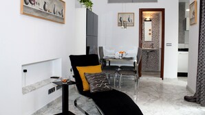 Een moderne woonkamer met een zwarte bank, een eethoek met een tafel en stoelen, en een keuken op de achtergrond.