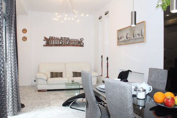 A modern living room with a sofa, dining table, chairs, and a chandelier.