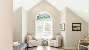 A room with a high ceiling, a large arched window, two armchairs, a small table, and a bench. - Storybook Stone Home | On the Bourbon Trail (Lawrenceburg)