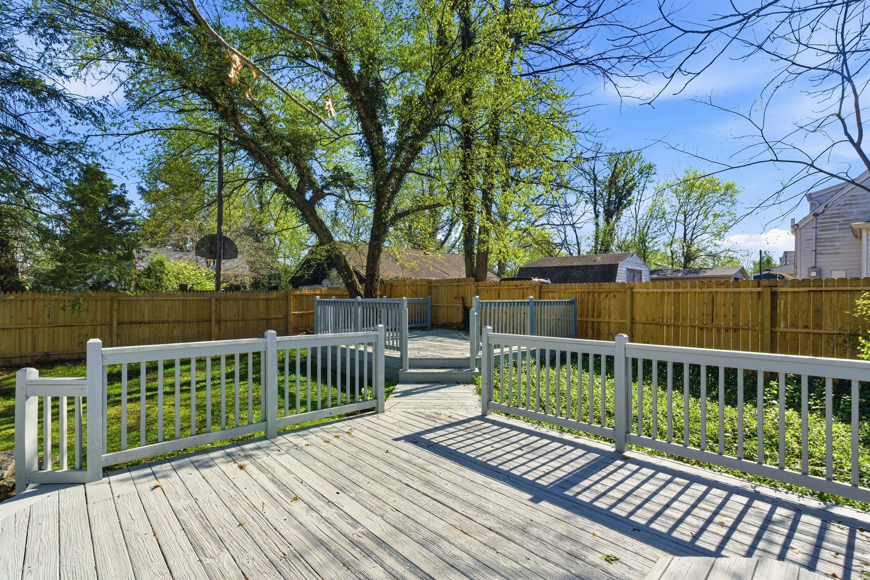 A wooden deck with white railings, surrounded by a wooden fence and trees.