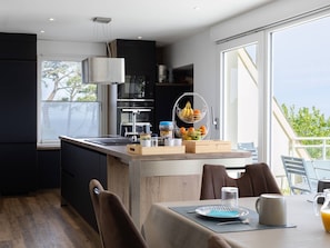 Een moderne keuken met een centraal eiland, een eethoek met tafel en stoelen, en grote ramen met uitzicht op de omgeving.