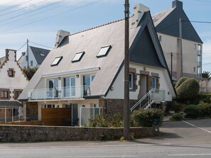 Een modern huis met een schuin dak, een balkon en een stenen muur ervoor.