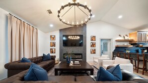 A modern living room with a fireplace, a large TV, and a dining area with wooden chairs. - Lakefront Sleeps 18 w/ Pool, Dock, Putting Green, Hot Tub! Hot Springs (Hot Springs)