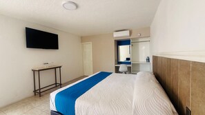 Una camera d'albergo con un letto, una TV a parete, un tavolino con uno specchio e un armadio.