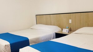 Quarto de hotel com duas camas de solteiro, cabeceira de madeira, mesa de cabeceira com uma garrafa de água e uma placa.