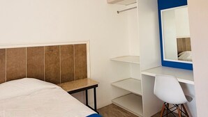 Quarto de hotel com cama, escrivaninha, espelho e ar condicionado.