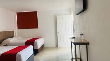A hotel room with two beds, a TV mounted on the wall, a door, and a small table with a bottle.