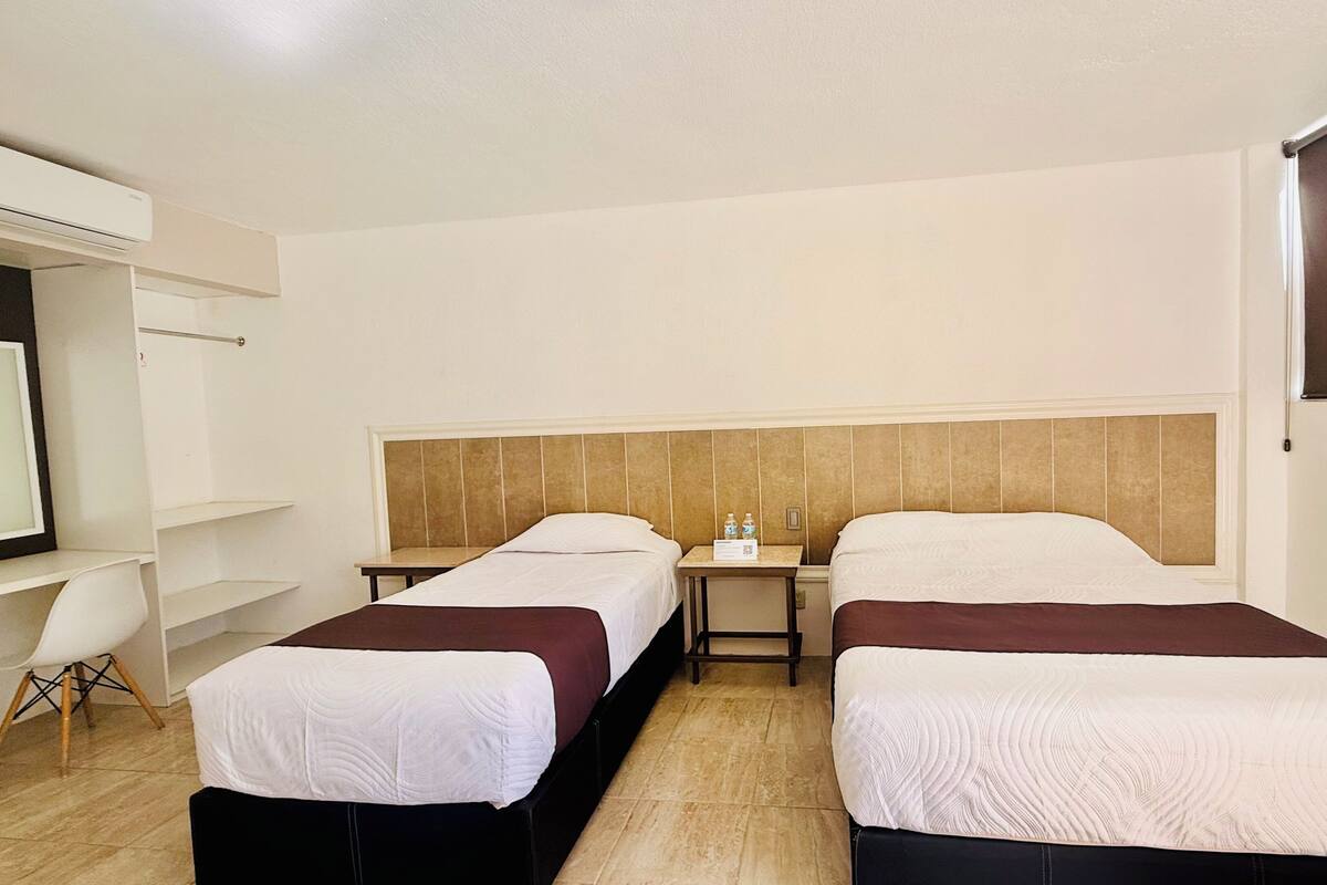 Habitación de hotel con dos camas, un escritorio, una silla y un televisor.