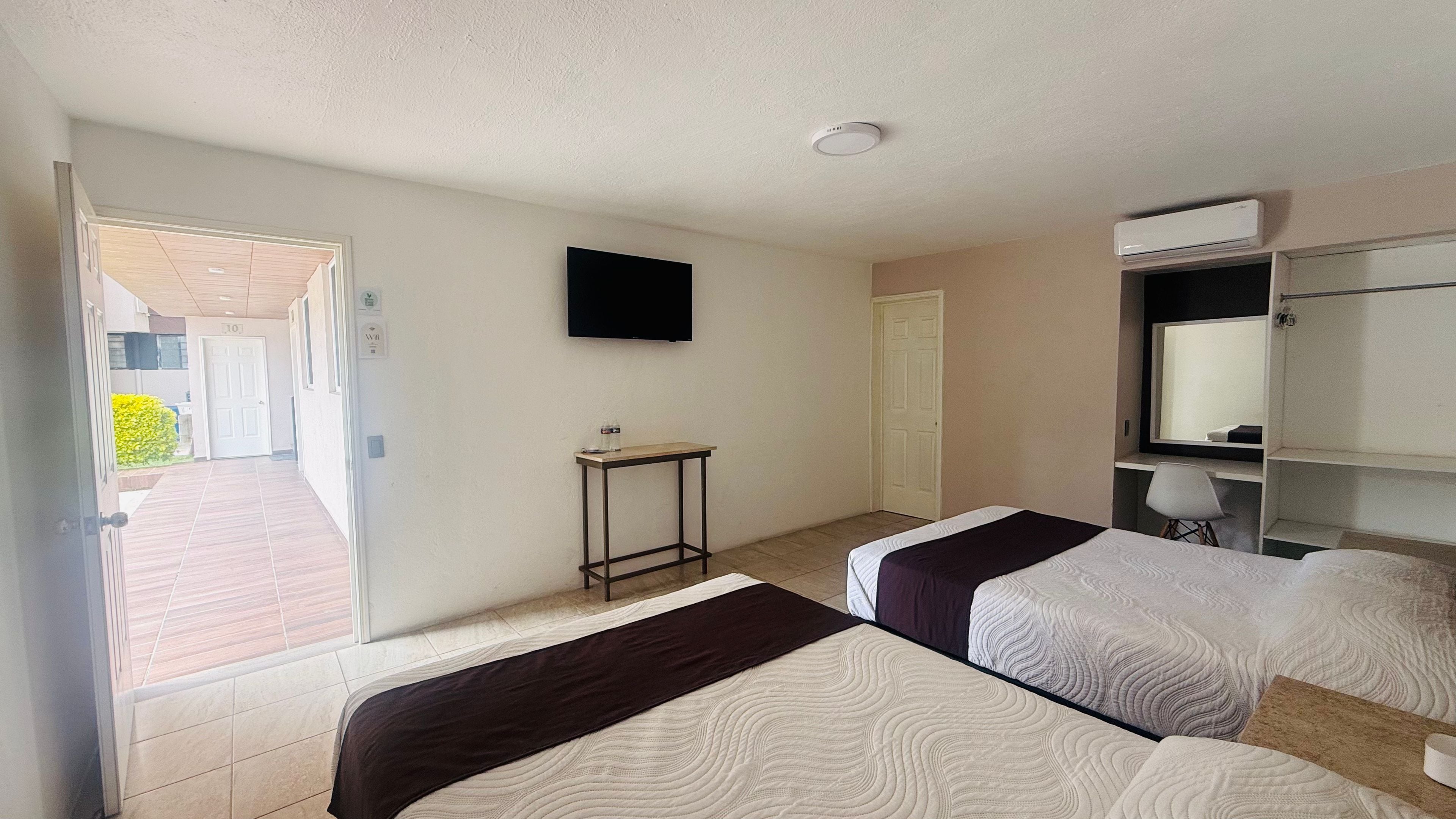 A hotel room with two beds, a small table, a TV, and a wardrobe.