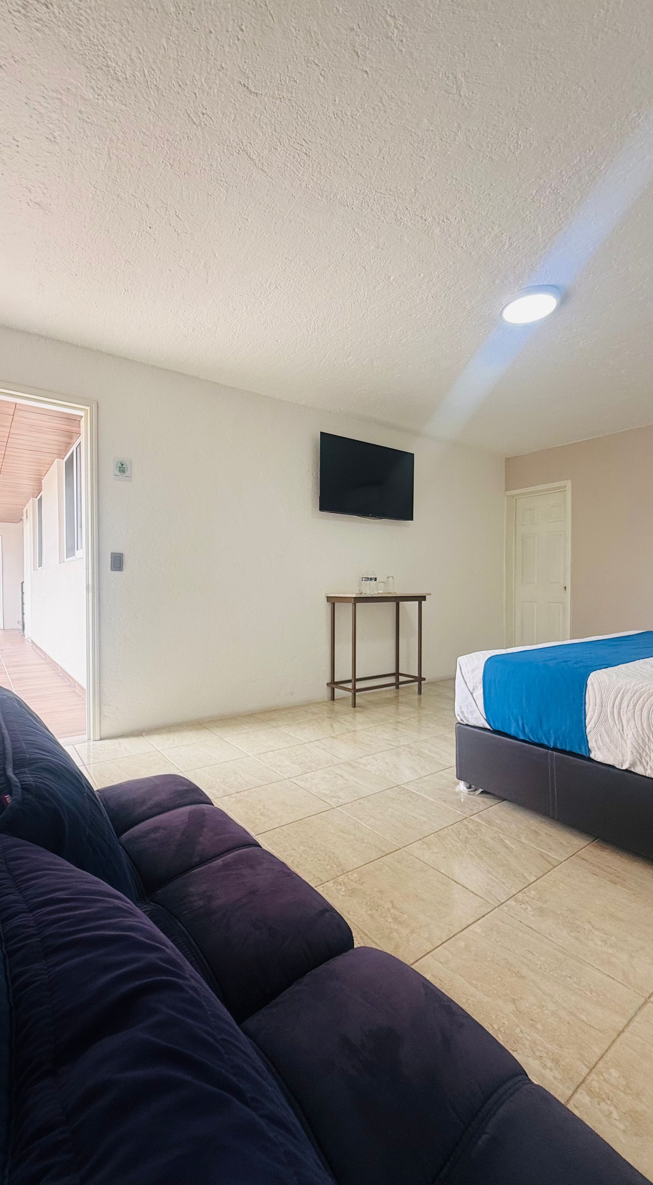A room with a bed, a television mounted on the wall, a small table, and a sofa.