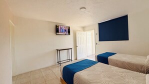Quarto de hotel com duas camas, uma televisão na parede, uma porta e uma pequena mesa.