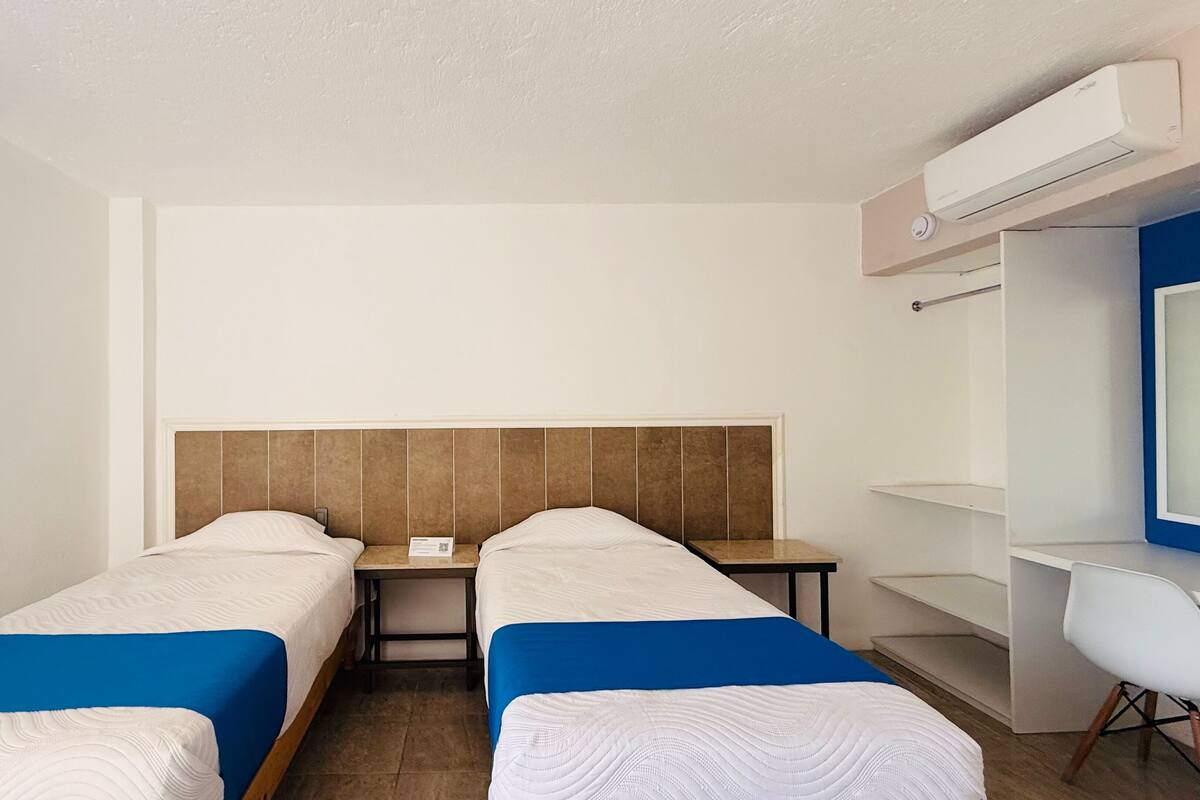 Una habitación de hotel con dos camas individuales, un escritorio, una silla y un armario.
