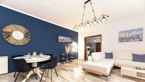 Uma sala de estar moderna com sofá, mesa de jantar e cadeiras. Há um quadro na parede e um abajur.