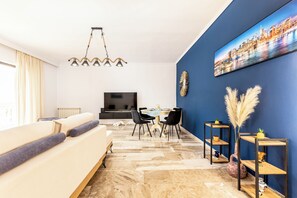 A modern living room with a sofa, dining table, chairs, a TV, and decorative items.