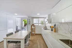 A modern kitchen with white cabinets, a wooden dining table, and a view of the outdoors. - Alcaidesa Golf and Beach Resort: Relaxation with Pool, Mountain Views and Prime Location (La Alcaidesa)