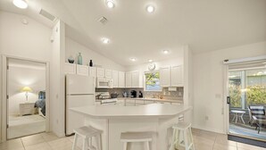 Een moderne keuken met witte kasten, een centraal keukenblok met krukken, een magnetron en een klok aan de muur.