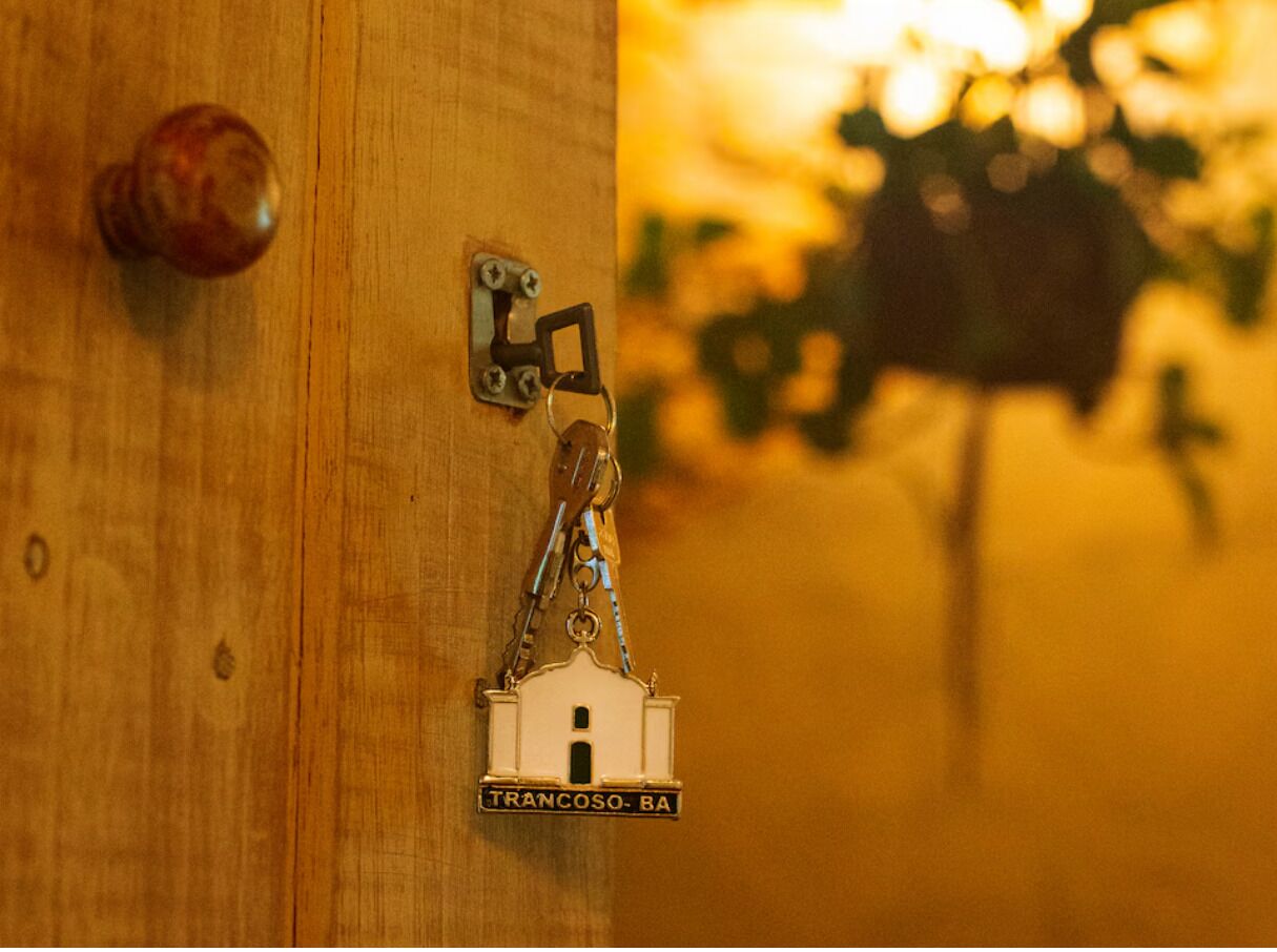 A wooden door with a keyhole and a keychain with a building-shaped key fob labeled 'TRANCOSO-BA'.