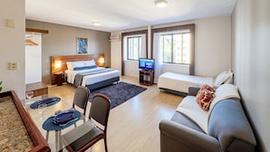 Ein Hotelzimmer mit Bett, einer Couch, einem Fernseher, einem Essbereich mit Tisch und Stühlen sowie einem Fenster.