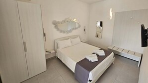 Quarto de hotel com cama, guarda-roupa, espelho e um banco.