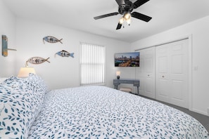 Une chambre à coucher comprenant un lit, un ventilateur de plafond, un bureau, une chaise, une télévision et une armoire.