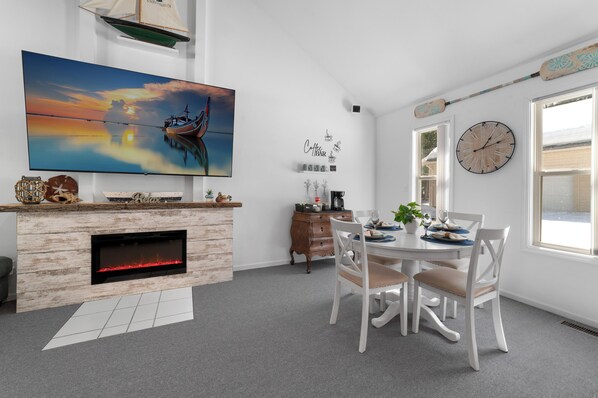 Ein modernes Wohnzimmer mit Kamin, Esstisch und großem, an der Wand befestigten Fernseher.