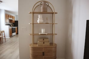 Un coin avec une étagère en bois à plusieurs niveaux, un vase blanc, une bougie et une petite boîte.