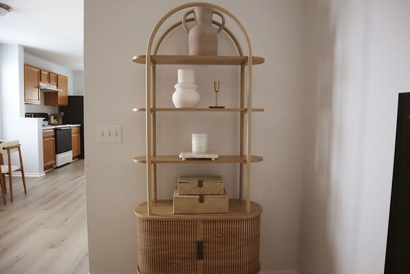 A corner with a wooden multi-tiered shelf unit, a white vase, a candle, and a small box.