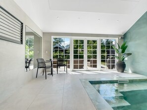 A modern indoor pool area with a clear view of the outside, a seating area with chairs, and a large potted plant. - "Goti" - 400m from the sea by Interhome (Væggerløse)