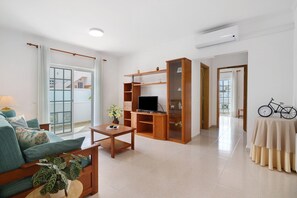 A living room with a sofa, coffee table, TV stand, and a bicycle. - Apartment 'Galego A' with Shared Pool, Shared Garden and Wi-Fi (Olhos de Água)