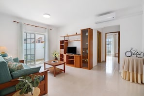 A living room with a sofa, coffee table, TV stand, and a bicycle. - Apartment 'Galego A' with Shared Pool, Shared Garden and Wi-Fi (Olhos de Água)