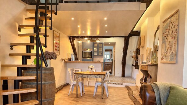 Ein modernes Interieur mit einer Holztreppe, einem Essbereich mit Tisch und Stühlen, einer Küche im Hintergrund und einem Ledersofa.