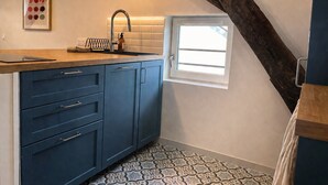 Eine Küche mit blauem Schrank, Spüle, Fenster und Fliesenboden.
