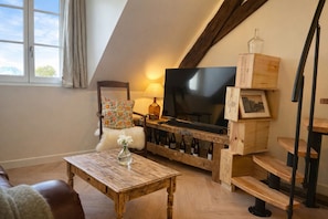 Een loft-achtige woonkamer met een houten tv-meubel, een bank, een salontafel en een trap.