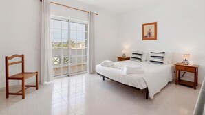 A bedroom with a bed, a chair, a nightstand, a picture on the wall, and a sliding door to the balcony. - Apartment 'Galego C' with Shared Pool, Shared Garden and Wi-Fi (Olhos de Água)