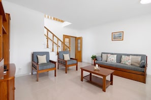 Ein Wohnzimmer mit einer Couch, zwei Sesseln, einem Couchtisch und einer Holztreppe.