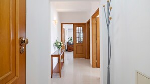 A hallway with a wooden door, a bench, a vase with flowers, and a wall-mounted light fixture. - Apartment 'Galego C' with Shared Pool, Shared Garden and Wi-Fi (Olhos de Água)