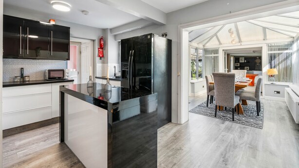 A modern kitchen with black appliances, white cabinetry, and a dining area with a table and chairs. - 6-bedroom home for contractors and families. (Colchester)