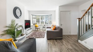 A modern living room with a sofa, armchair, TV, and a large window. - 6-bedroom home for contractors and families. (Colchester)